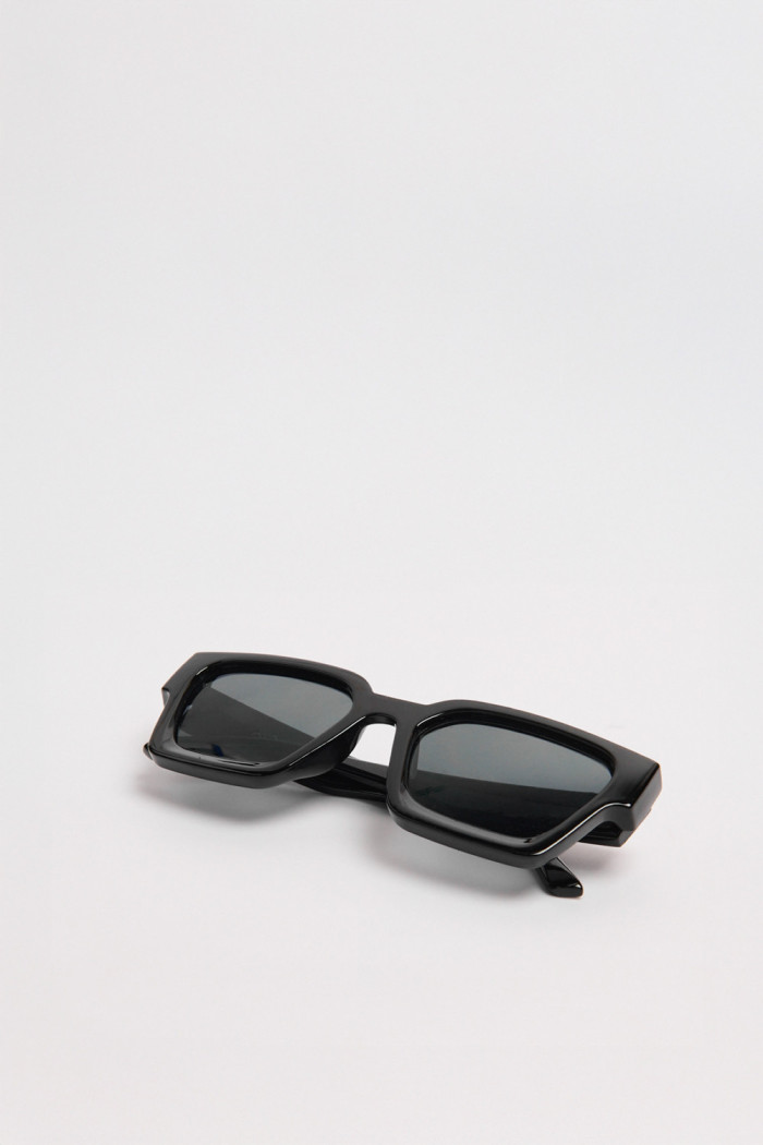 Gafas de sol con marco rectangular en color negro y lentes esfumados en contraste.