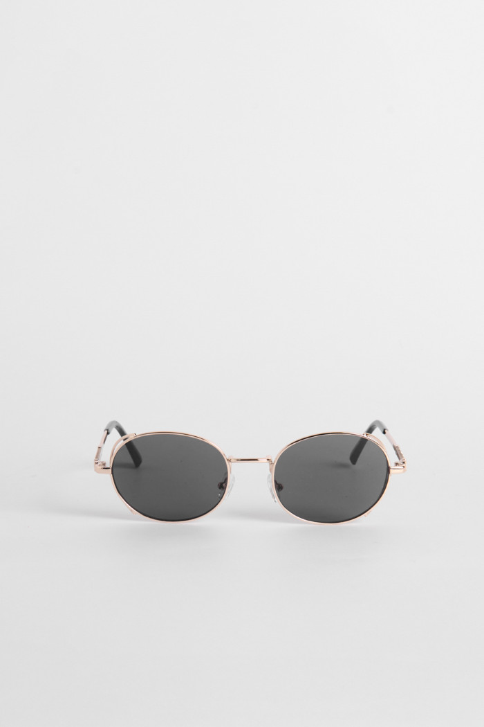 Gafas de sol con marco redondo dorado y lentes esfumados en contraste.