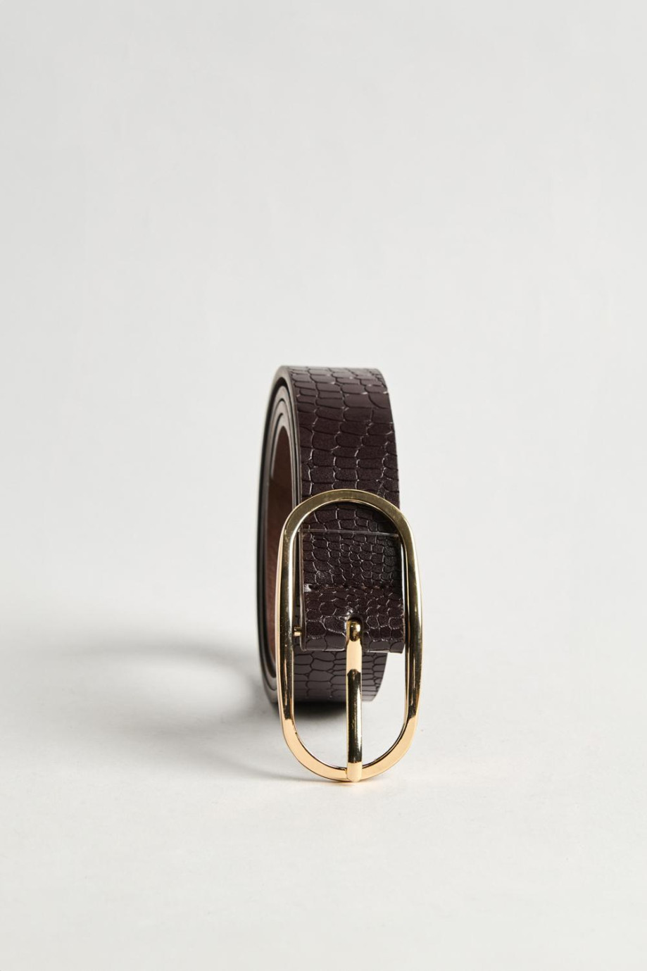 Cinturón femenino en color café oscuro, elaborado en sintético con textura tipo reptil, hebilla metálica ovalada y punta con for