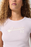 Camiseta para mujer en tela acanalada, cuello redondo y manga corta. Silueta ajustada con arte estilo college